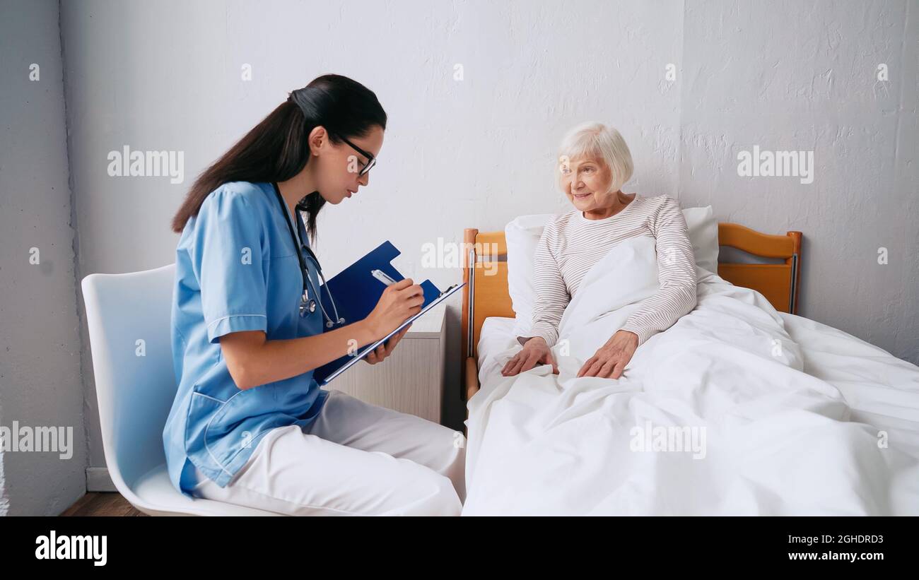 nurse in eyeglasses writing prescription in clipboard near