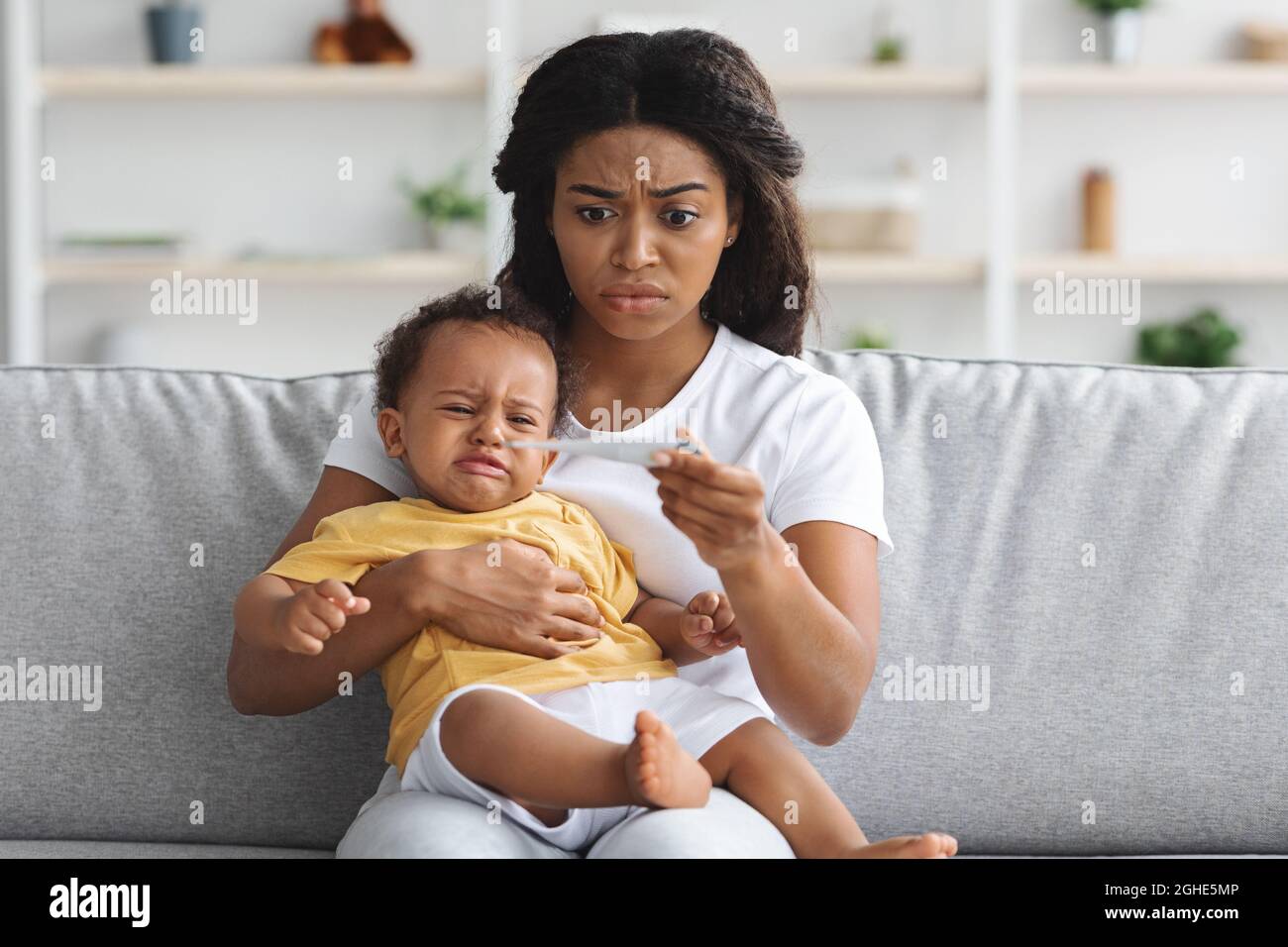 Worried Black Mother Checking Temperature Of Her Crying Infant Baby At Home Stock Photo