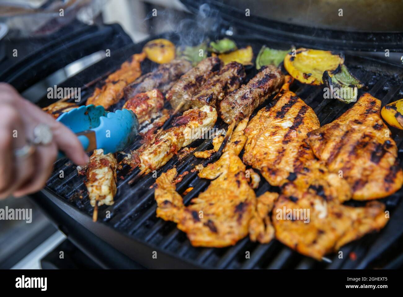 A person uses tongues to turn chicken and lamb cooking outdoors on a barbeque in London, England. Stock Photo