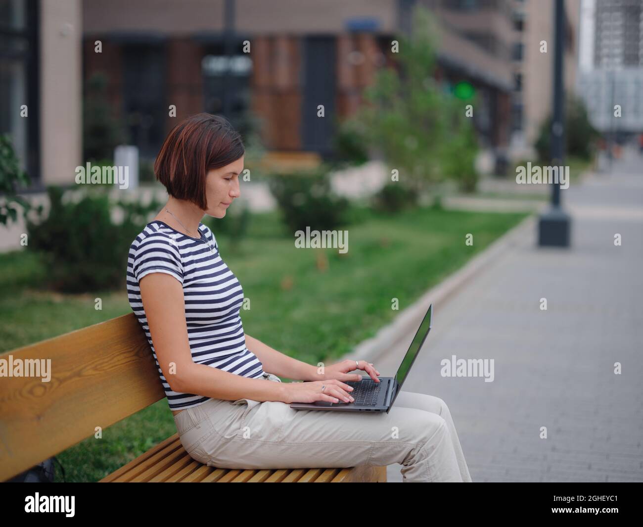 Young asian female student working at laptop sit down on bench outside ...