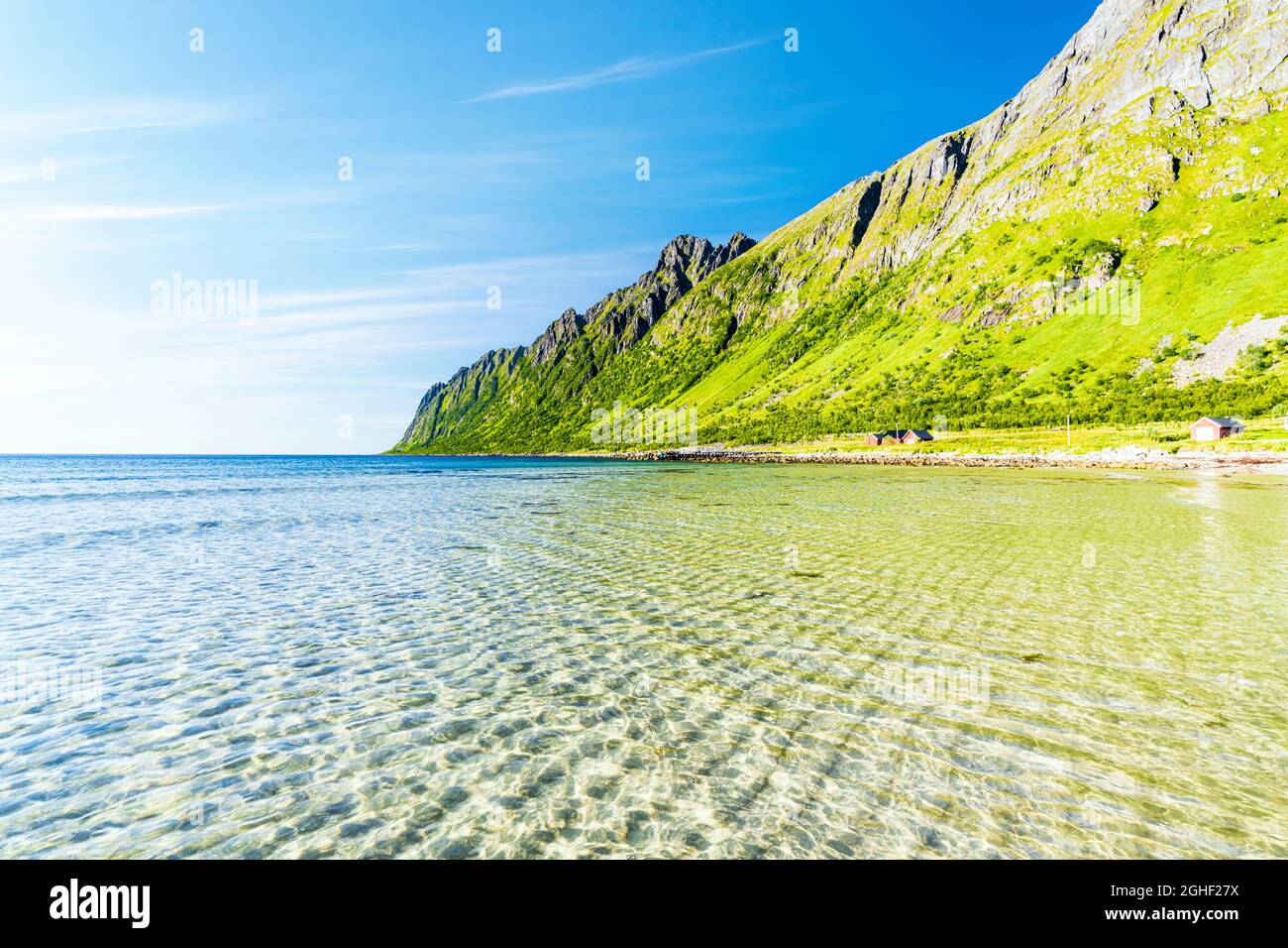 Rorbu at mountains feet on shore of the crystal turquoise sea at Ersfjord beach in summer, Senja, Troms county, Norway Stock Photo