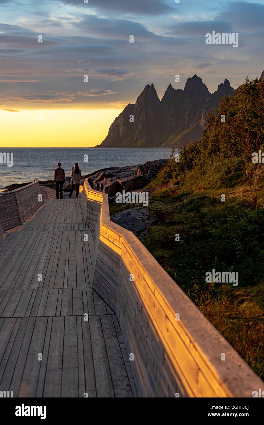 Girls with smartphone photographing the midnight sun standing on walkway, Tungeneset viewpoint, Senja, Troms county, Norway Stock Photo