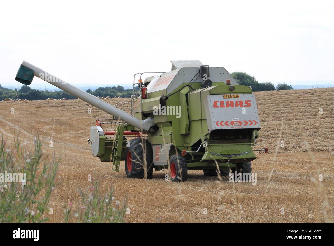 Farm machinery, a combine harvester in a cornfield harvesting hay with round straw bales on a