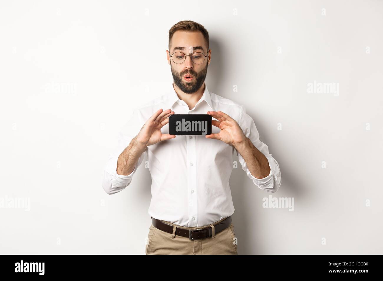 Amused handsome guy showing mobile screen, looking excited at online ...