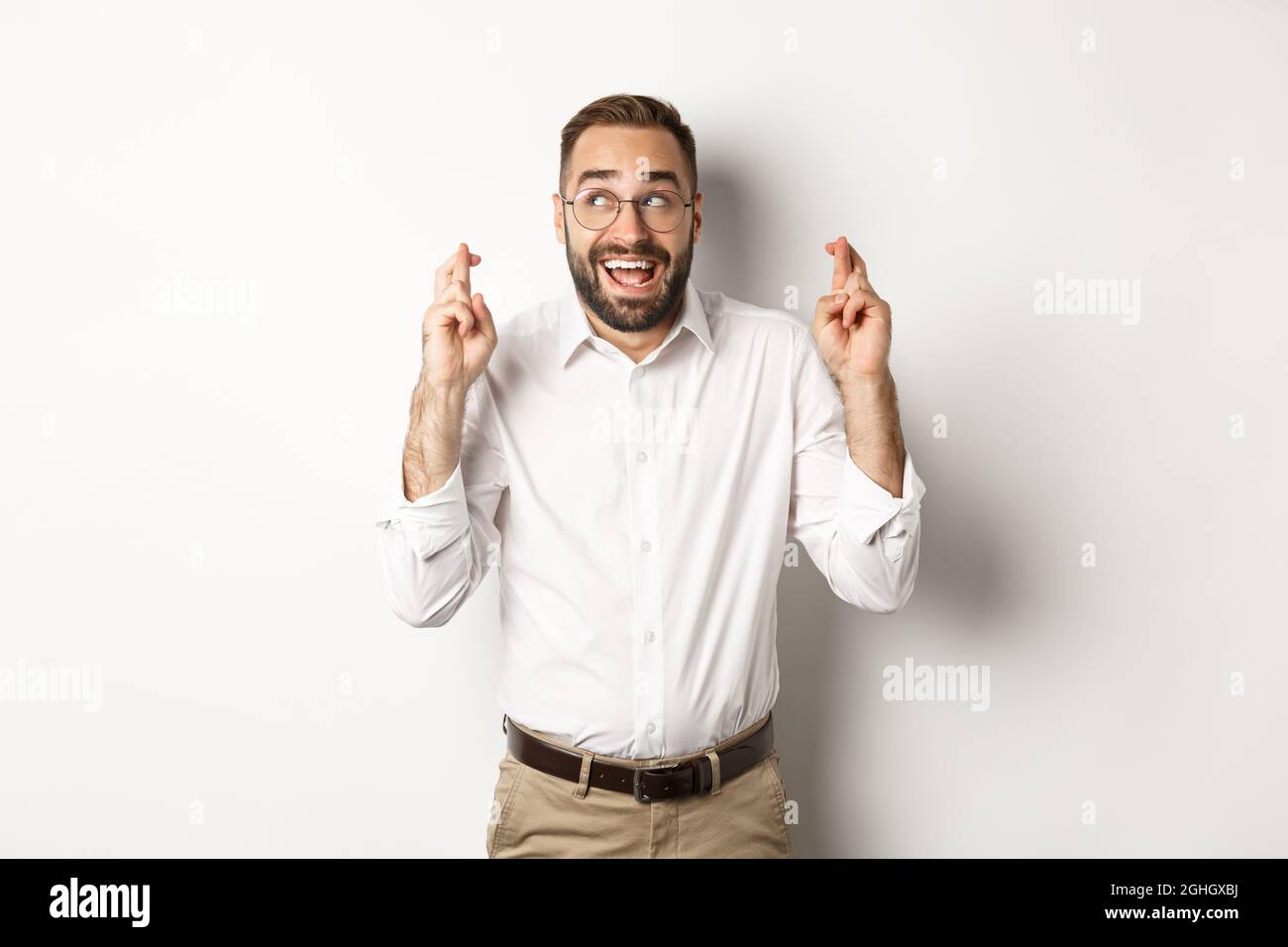 Excited and hopeful businessman making a wish, cross fingers and waiting, standing over white background Stock Photo