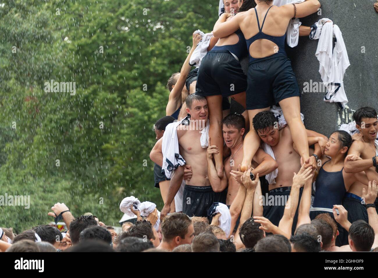 U.S Naval Academy midshipmen from the 2023 class struggle to climb the greased Herndon Monument to retrieve a hat symbolizing the successful completion of the freshman year August 22, 2021 in Annapolis, Maryland. Due to restrictions set forth by the COVID-19 pandemic, the Class of 2023 had to delay the tradition from May to August. Stock Photo