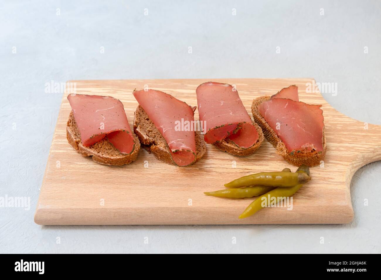 Sandwich with sliced dried meat served on cutting board on neutral grey background Stock Photo