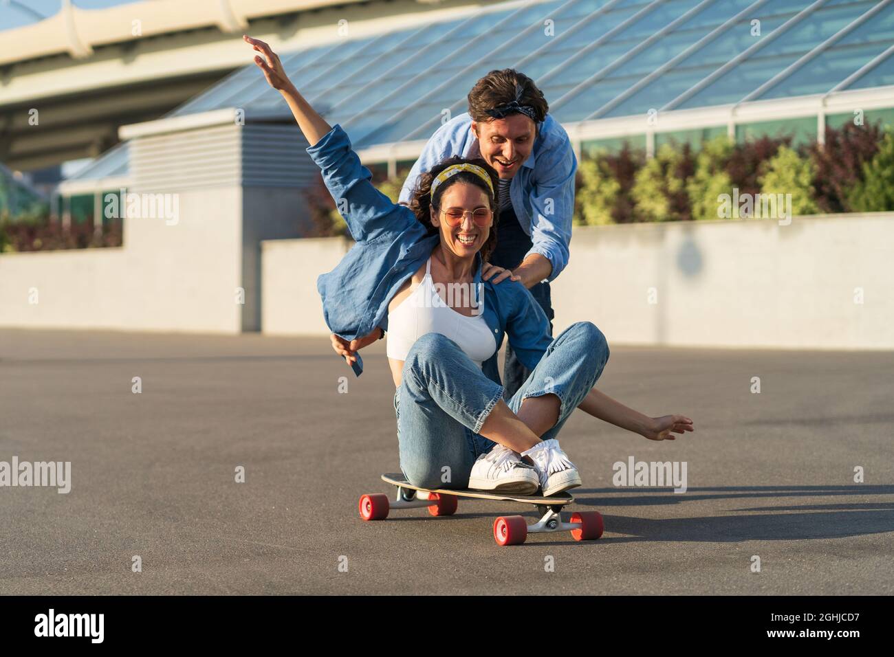 Couple have fun on longboard: male push back of joyful female sitting on  skateboard and laughing Stock Photo - Alamy