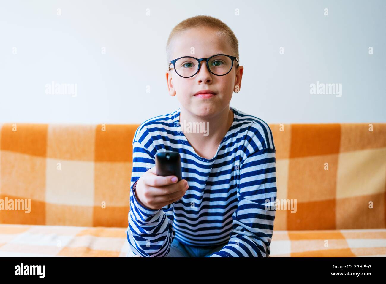 Teenage boy watching tv with glasses using tv remote while sitting on