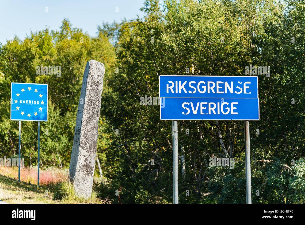 State border between Norway and Sweden in Northern Sweden, mountains in Lappland. Mile stone with Swedish text and blur road sign with Norwegian words Stock Photo