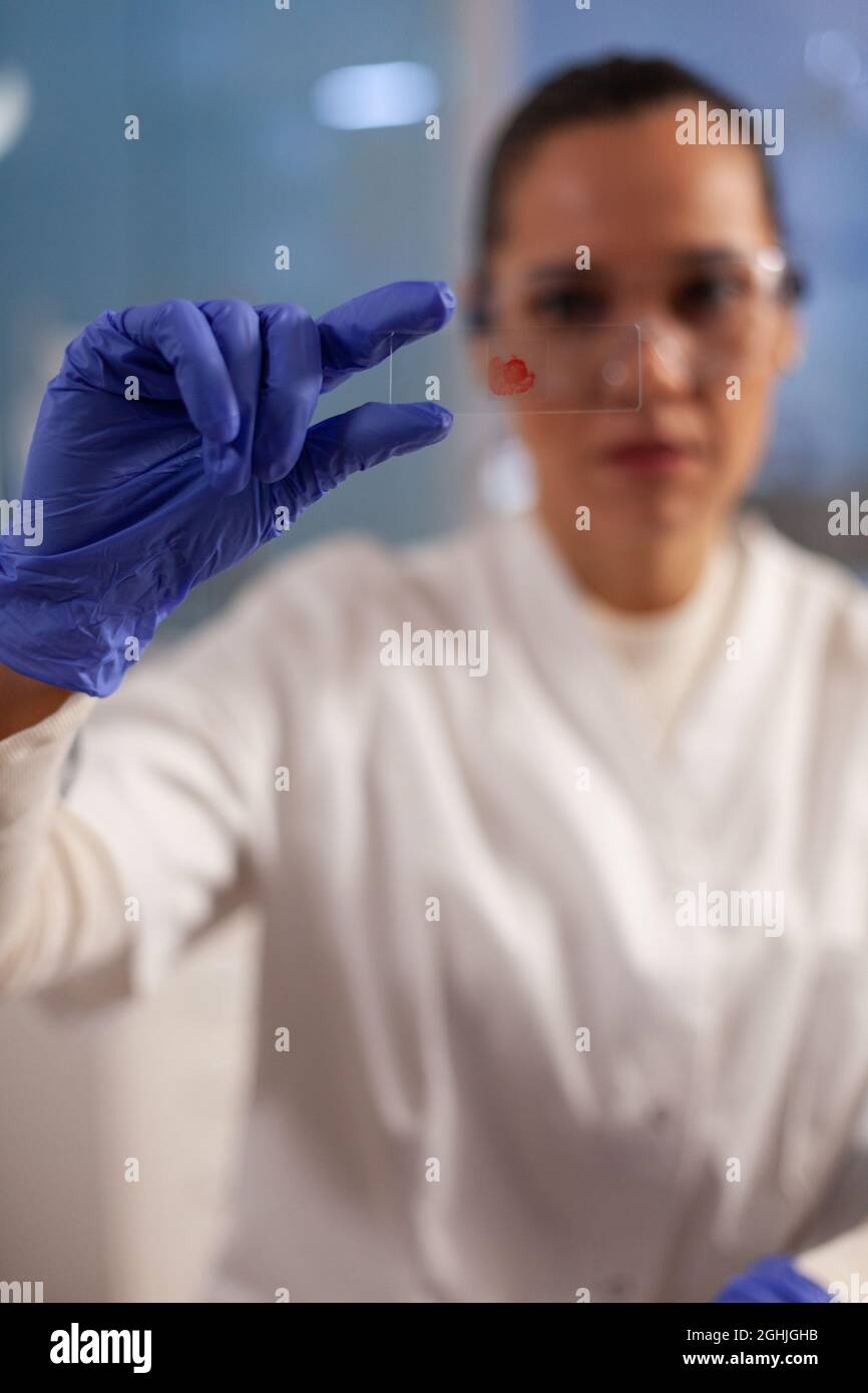Laboratory worker analyzing blood sample on glass for research activity at laboratory clinic. Professional woman working on chemical tests to develop scientific healthcare treatment Stock Photo