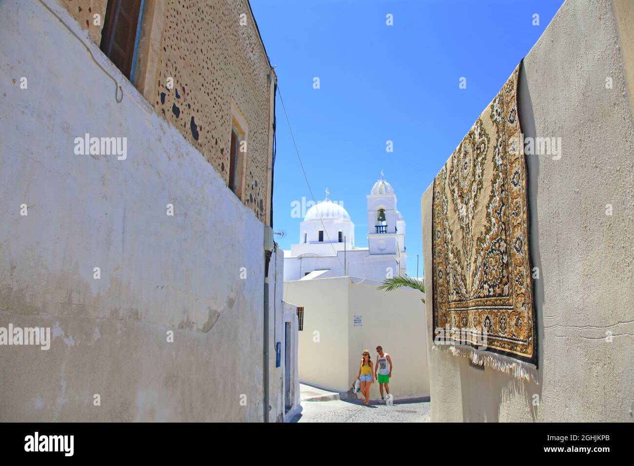 A carpet hanging on a wall with a white church in the background in the traditional village of Megalochori in Santorini, Greece. Stock Photo