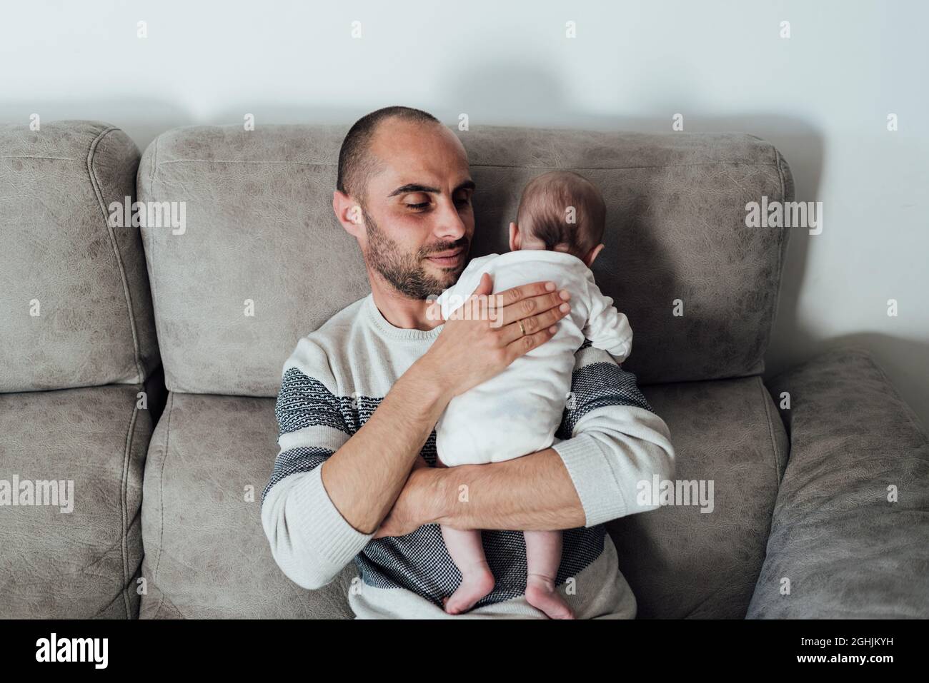 Father holding a baby in his arms while sitting on a sofa at home. Stock Photo