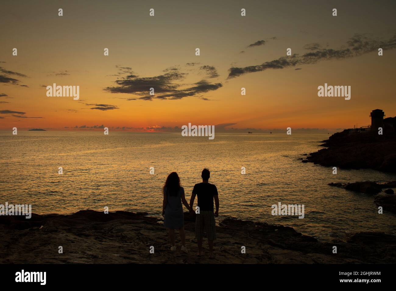 silhouettes of man and woman together on a mountain above the sea ...
