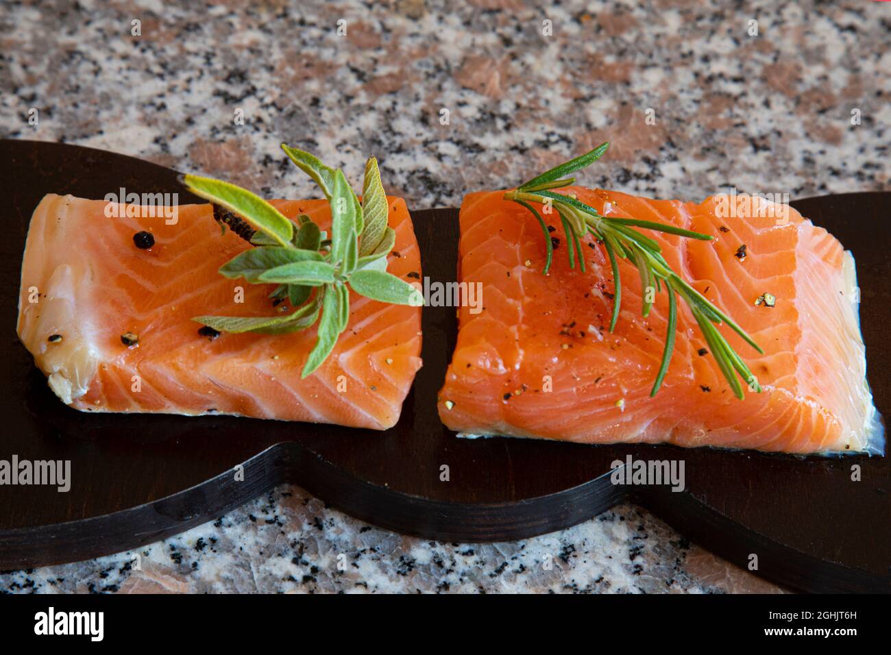 pieces of pickled salmon on a wooden board on a marble background, decorated with sage and rosemary leaves Stock Photo