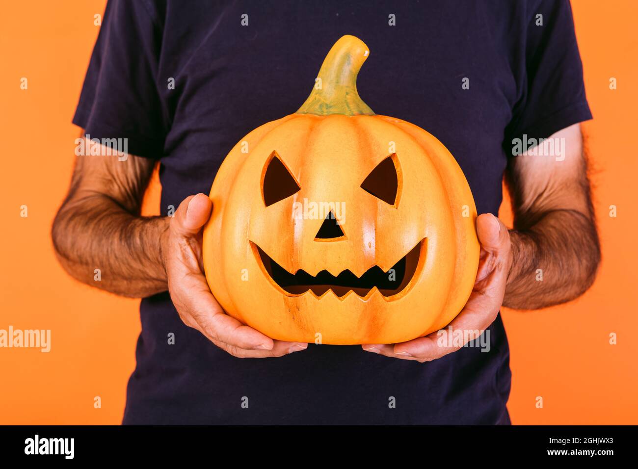 Detail of a terrifying pumpkin 'Jack-o-lantern' held by hands on an orange background. Halloween and days of the dead concept. Stock Photo
