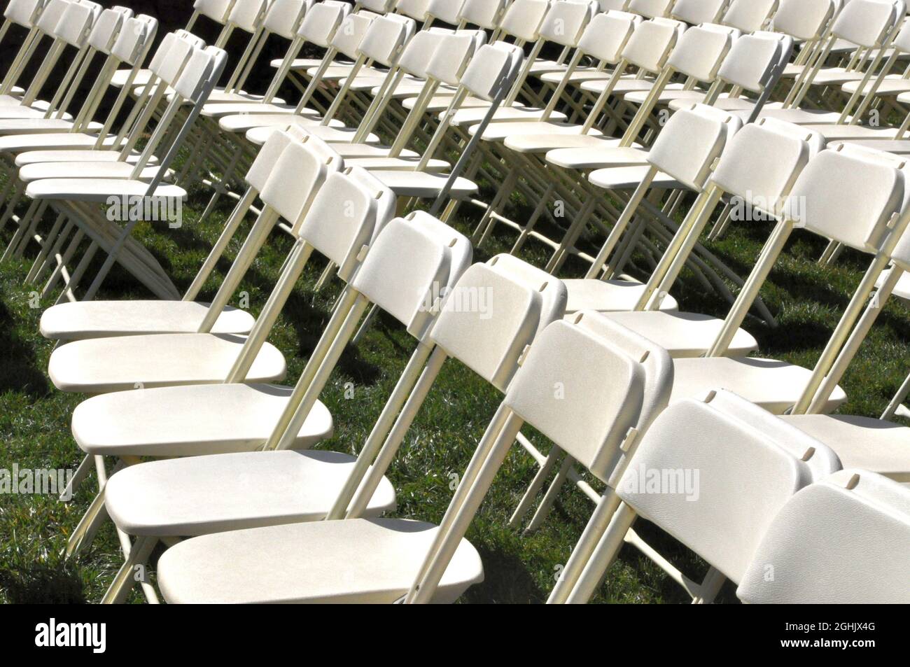 Lines of empty white folding chairs set up in grass in preparation for