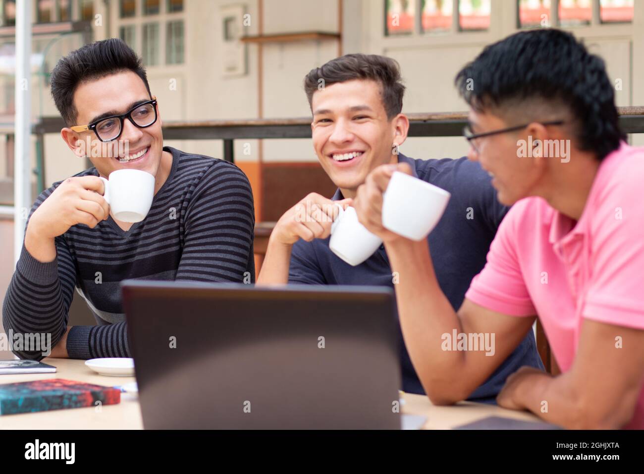 Three young students drinking coffee outdoors while talking and laughing. Stock Photo