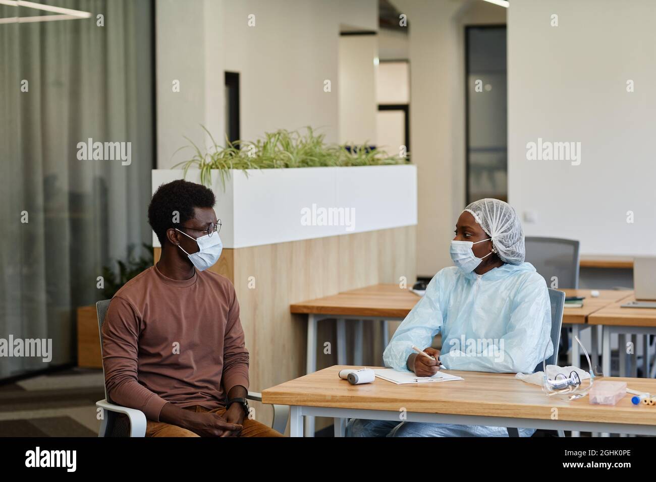 Medical nurse in protective suit and medical mask talking to patient ...