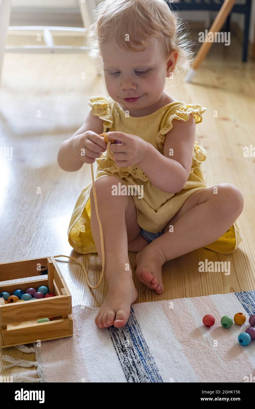 Smiling girl playing wooden removable beads for development of fine