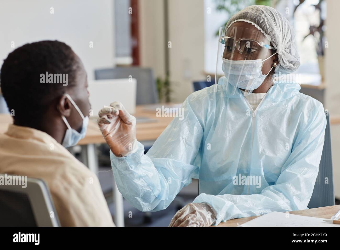Medical nurse in protective suit and face shield telling patient to be ready for nasal swab for coronavirus testing Stock Photo