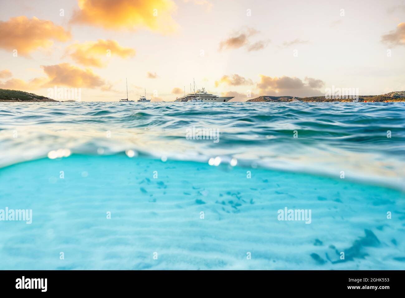 (Selective focus) Split shot, over under picture. Half underwater half sky with a luxury yacht sailing on a turquoise water during a stunning sunrise. Stock Photo