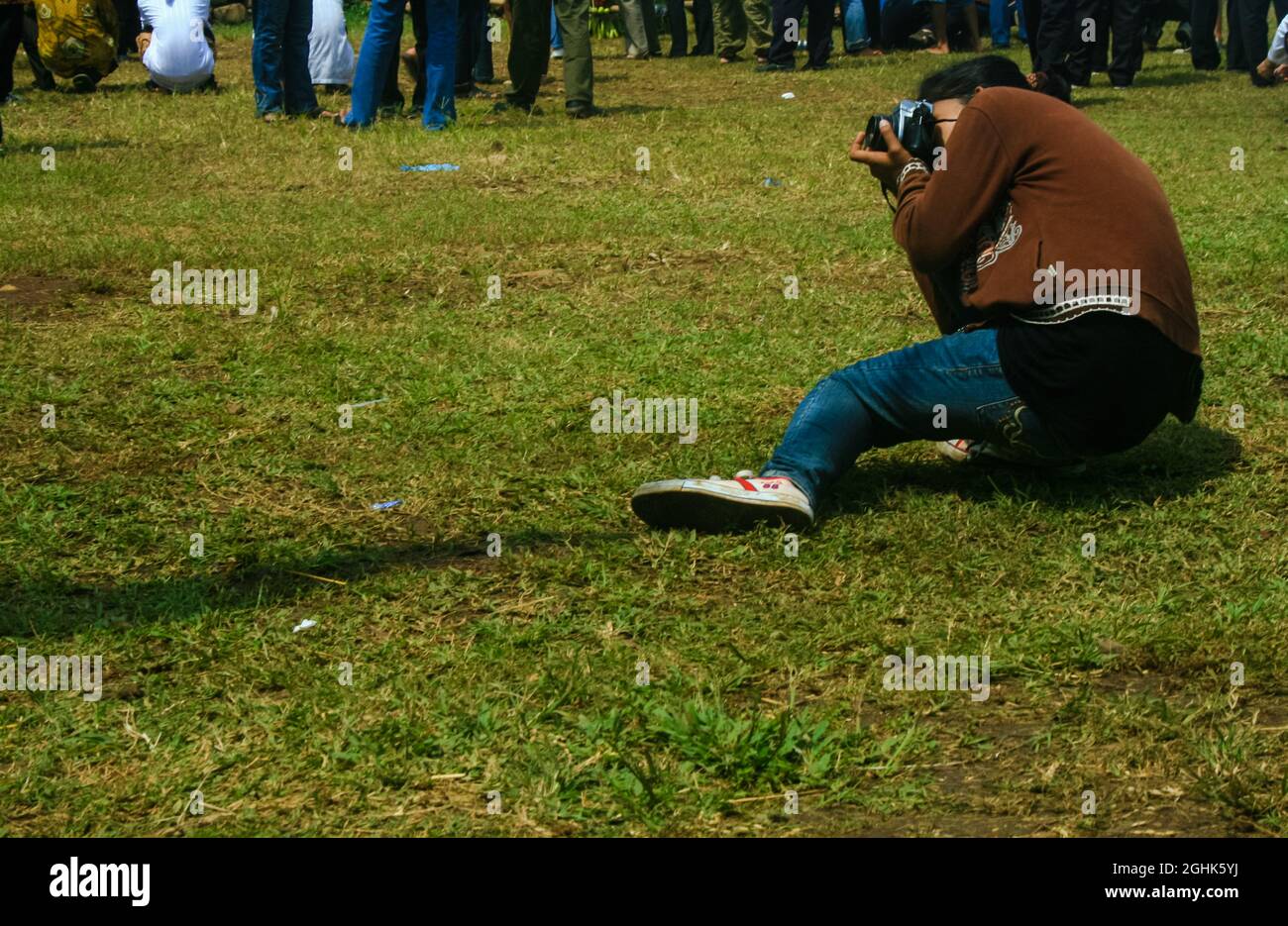 A person in a grassy field is photographing something until his body is lowered and his legs are bent. Stock Photo