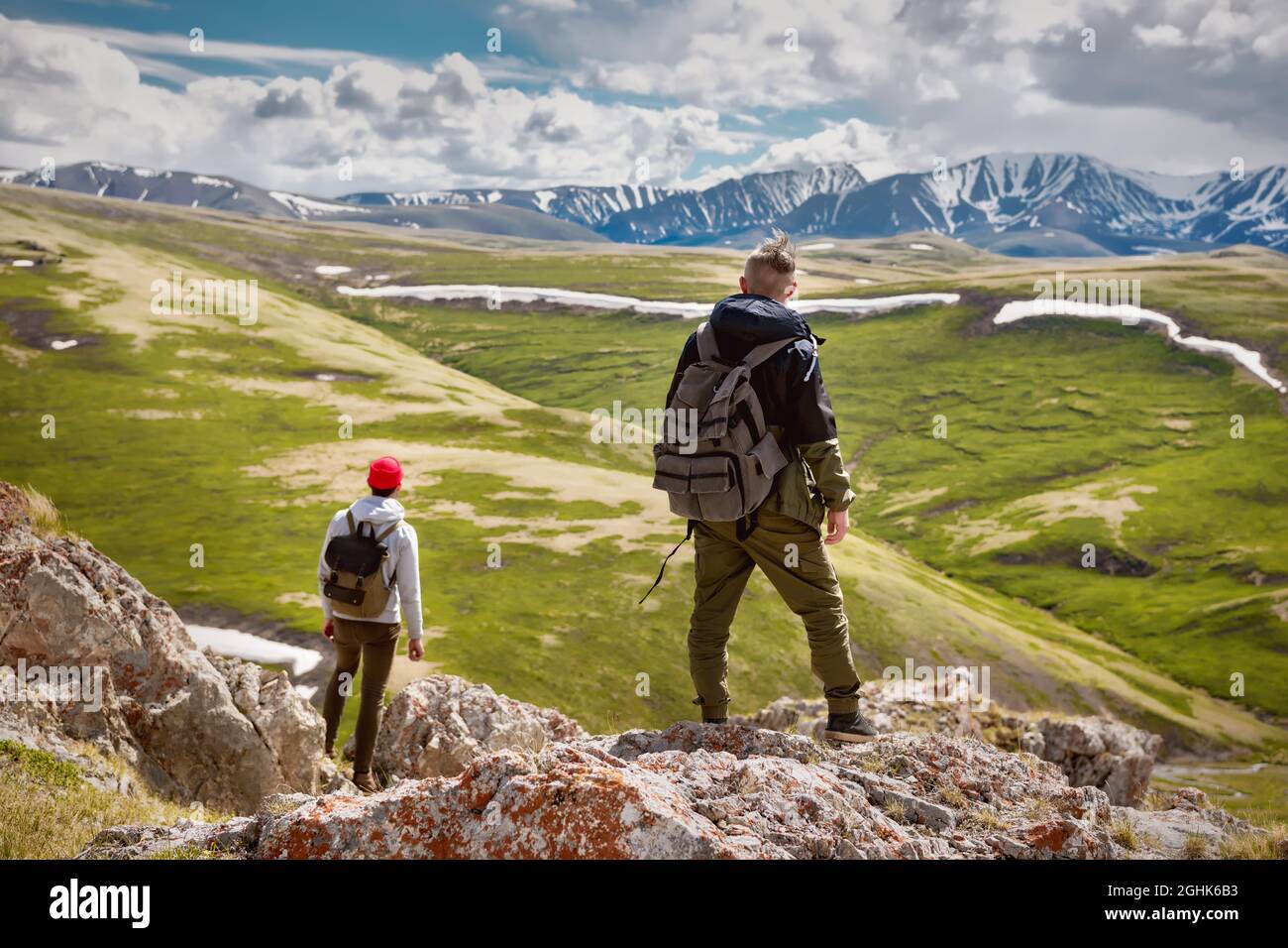 Two guys hikers stands with small backpacks and enjoys mountains valley view Stock Photo