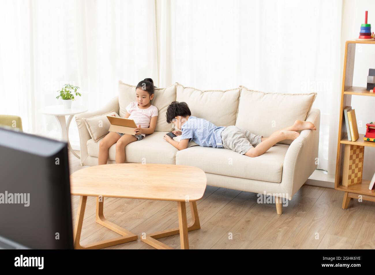 Cute children using digital devices on sofa Stock Photo