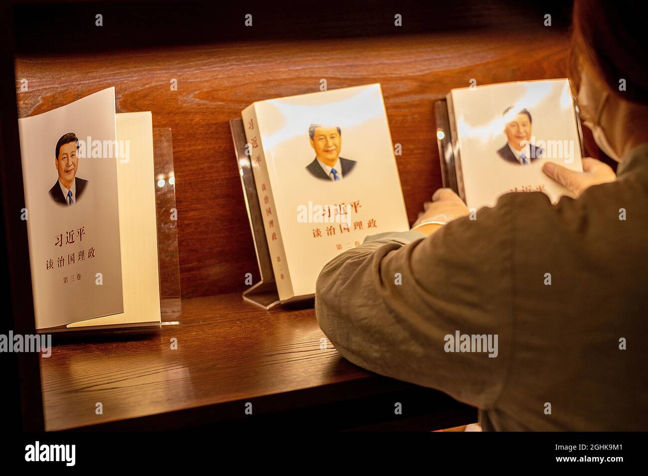 A waitress sorts out copies of  'Xi Jinping: The Governance of China' on the bookshelf at restaurant in Beijing, China. 07-Sep-2021 Stock Photo