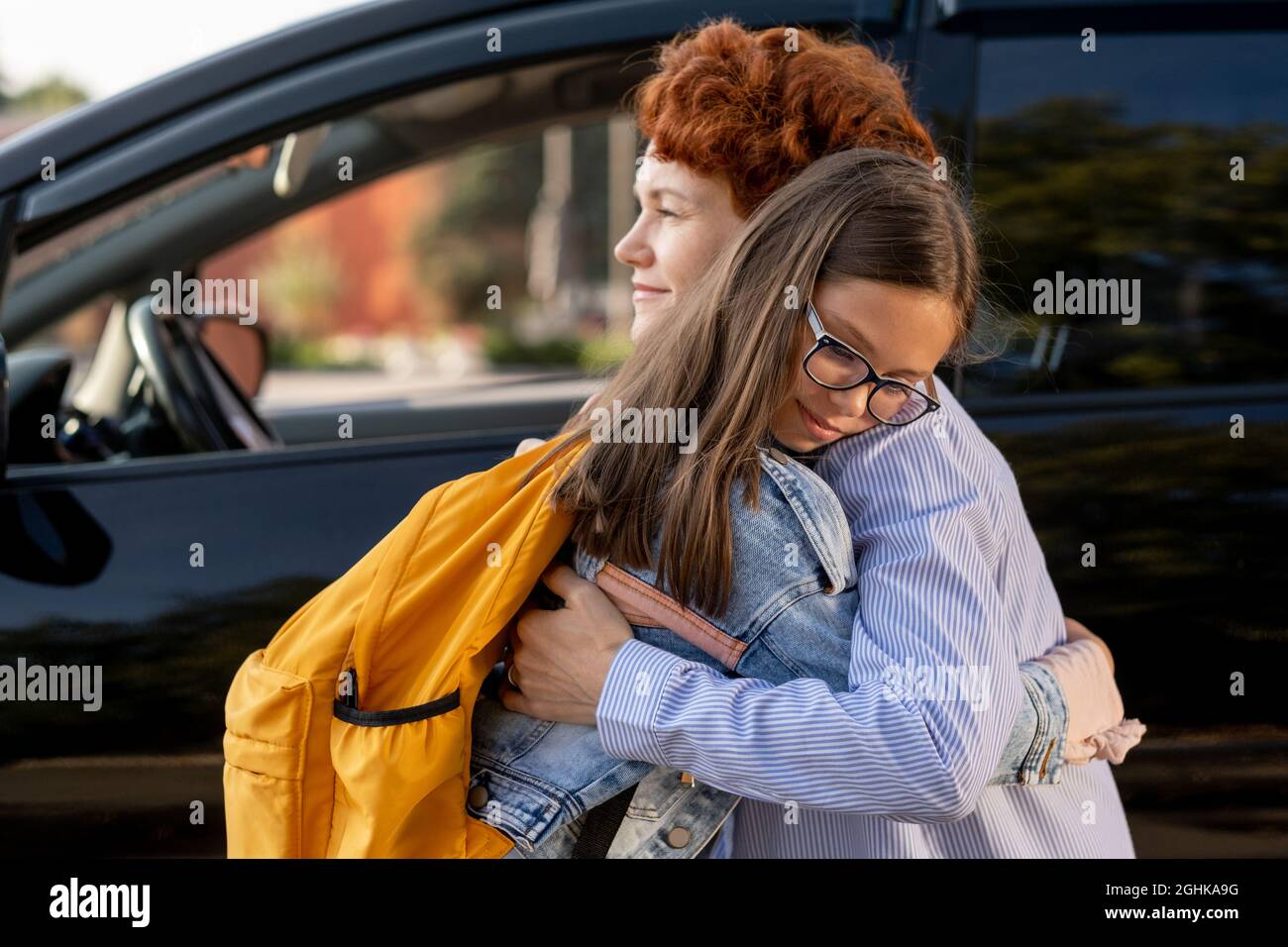 Mother and daughter standing in embrace against car outdoors in the morning Stock Photo