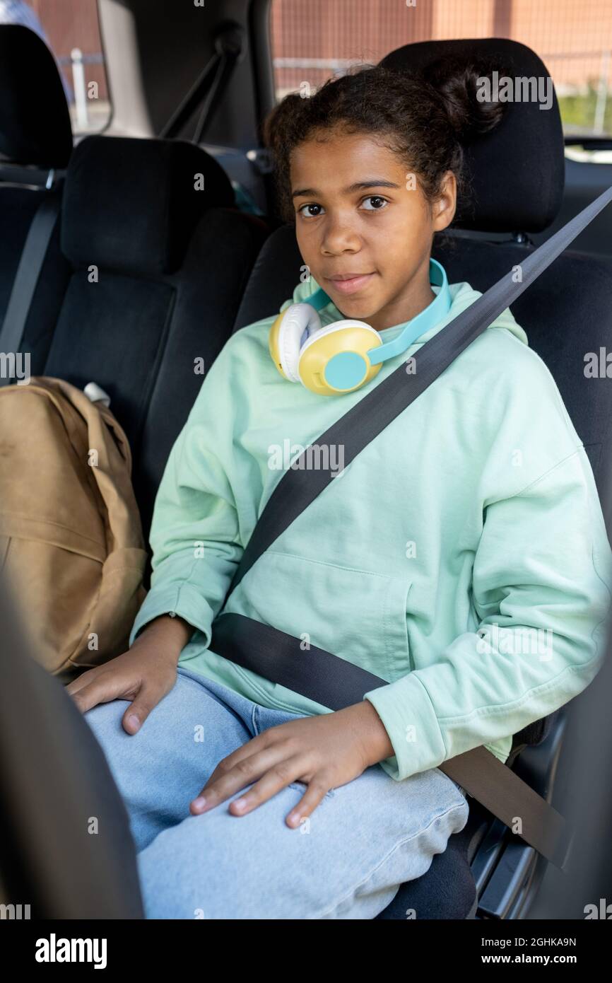 Cute mixed-race schoolgirl in casualwear sitting on backseat of car ready to go to school Stock Photo