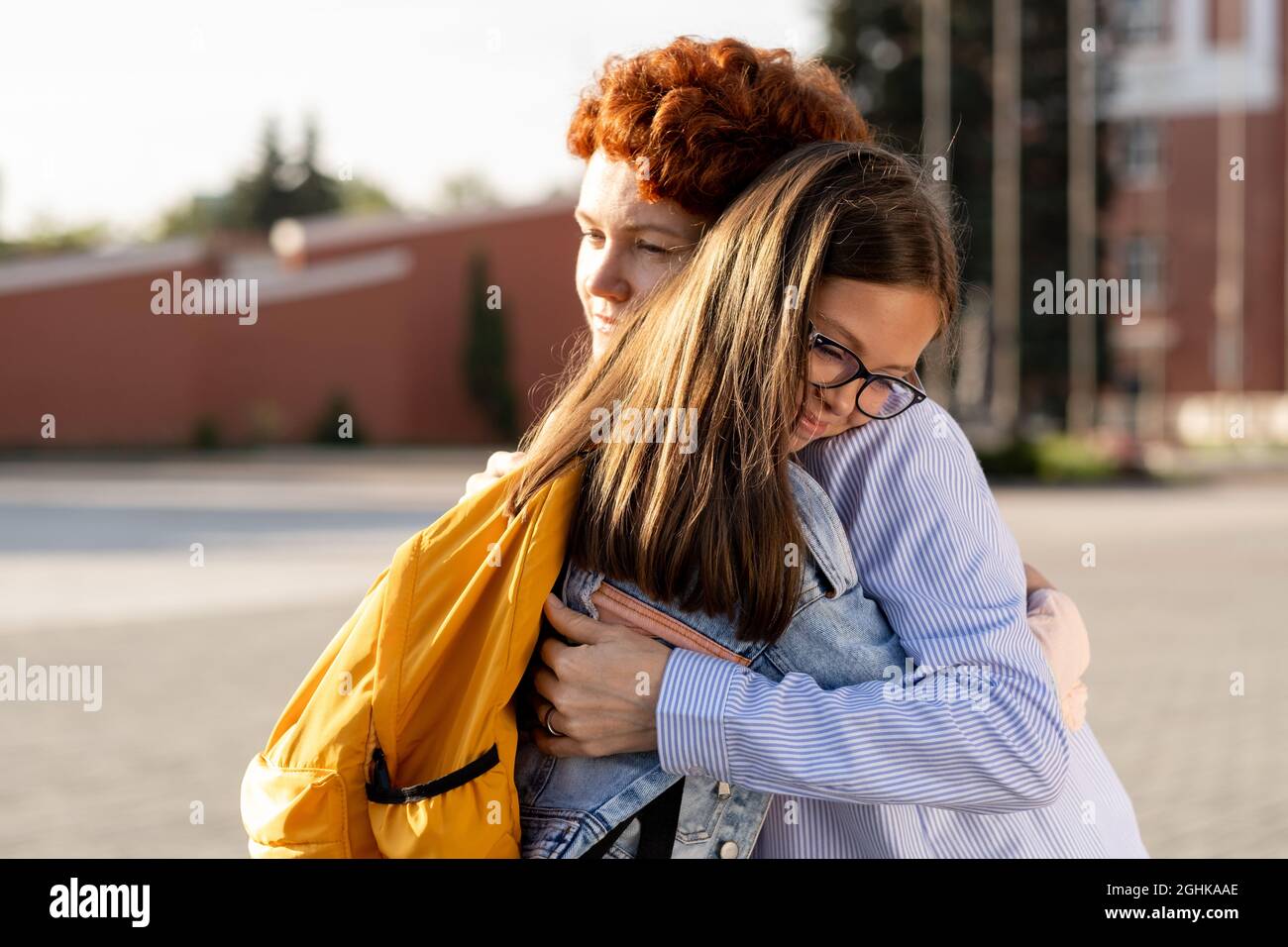 Young woman seeing off her youthful daughter with backpack while both standing in embrace Stock Photo