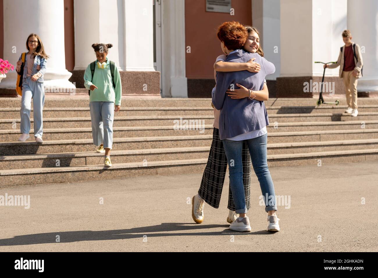 Happy and affectionate mom and daughter embracing by school building in the morning Stock Photo