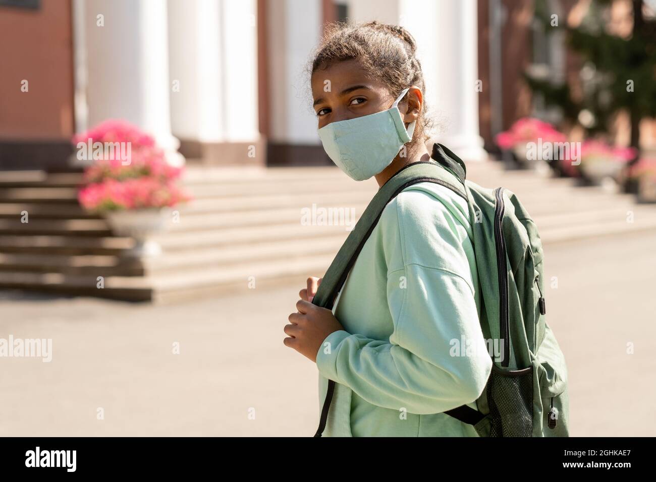 Contemporary mixed-race schoolgirl in protective mask looking at you while going to school Stock Photo