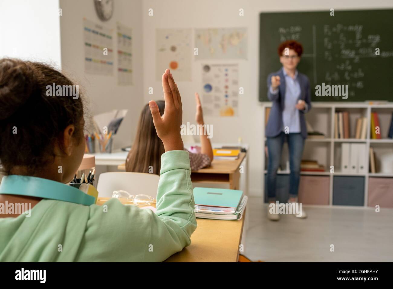 Rear view of African schoolgirl raising hand while teacher pointing at ...