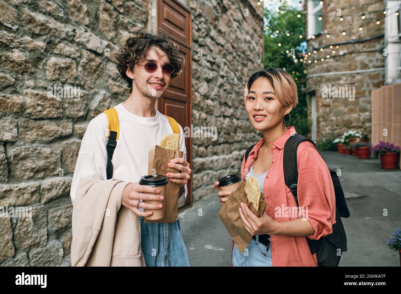 Happy young intercultural couple having fastfood with drinks in urban environment Stock Photo
