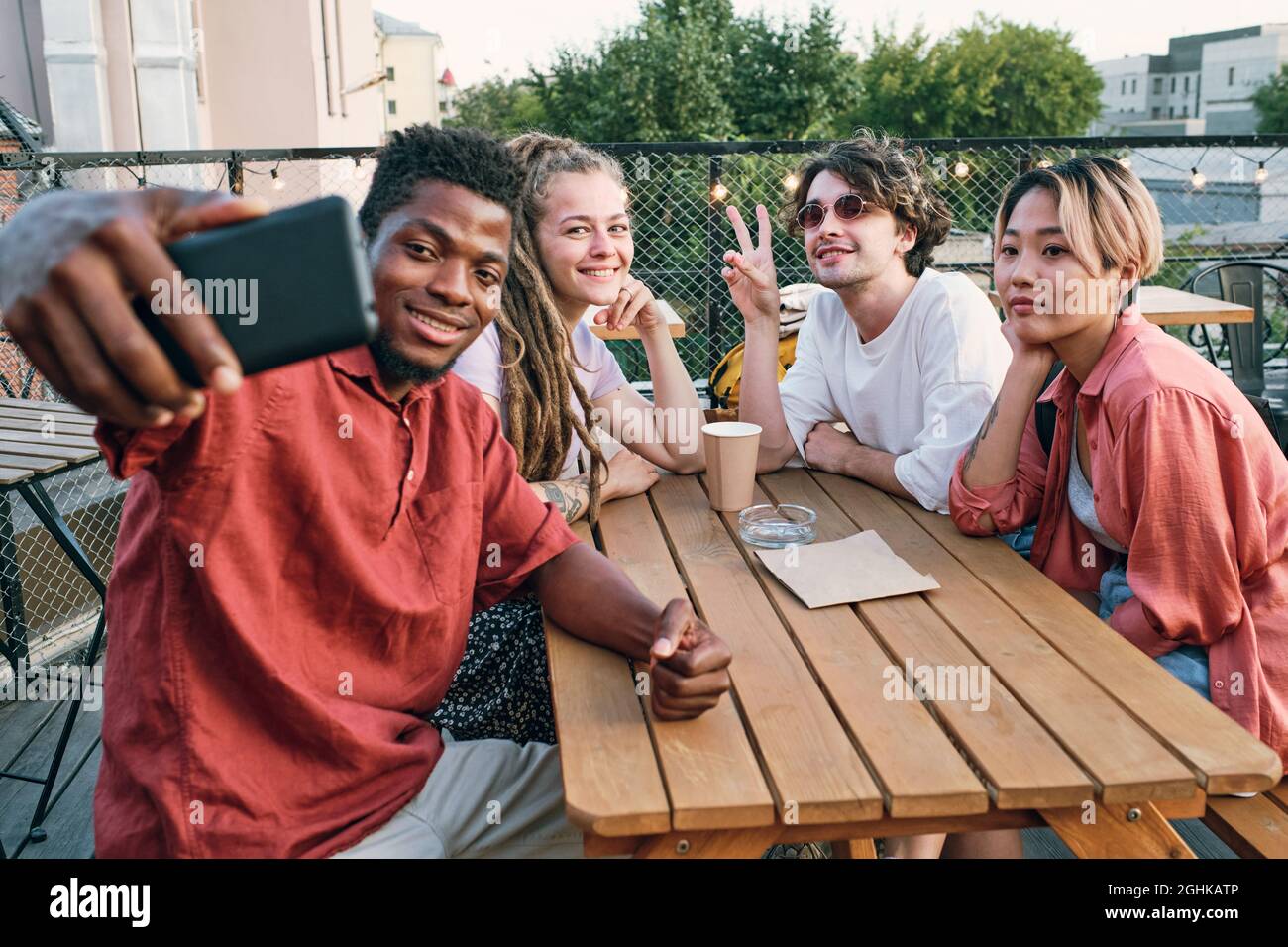 Happy African guy making selfie with intercultura friends by wooden table in urban environment Stock Photo