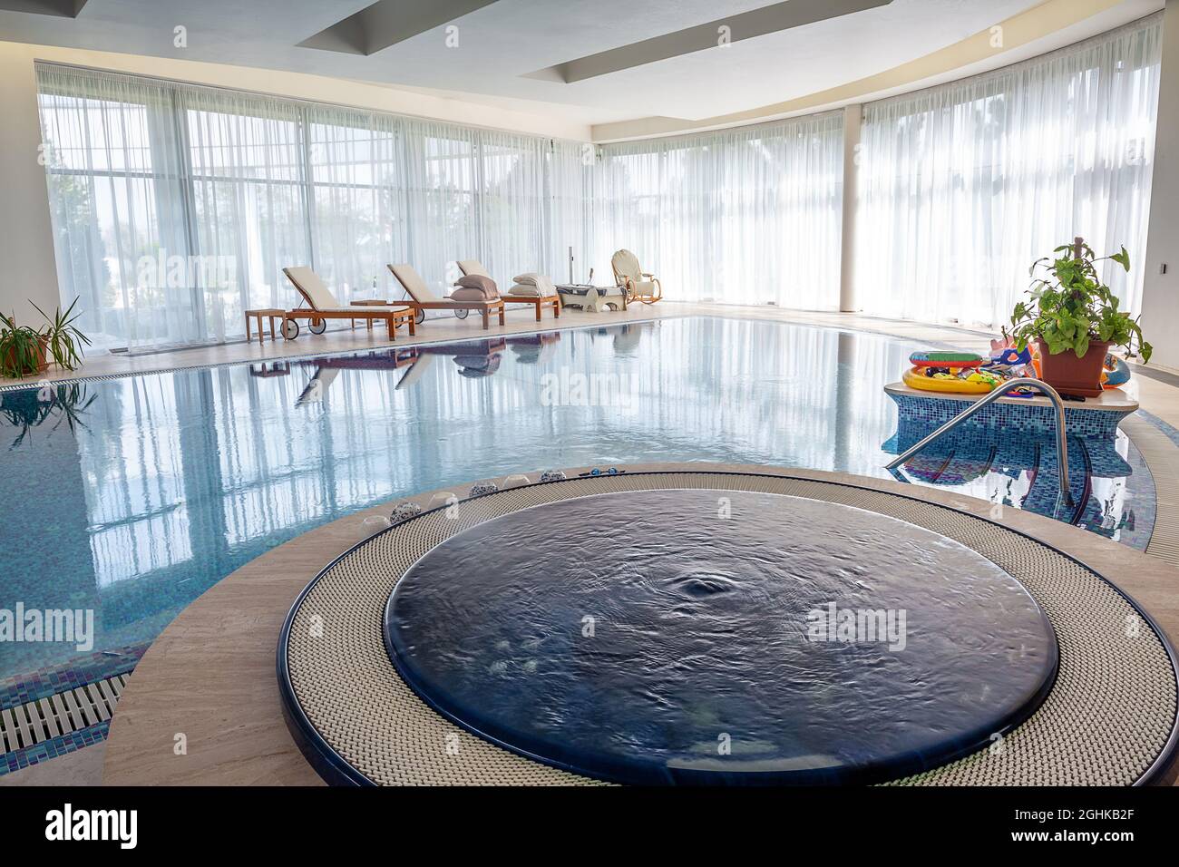 Relaxation area near indoor swimming pool with jacuzzi and loungers in country mansion Stock Photo