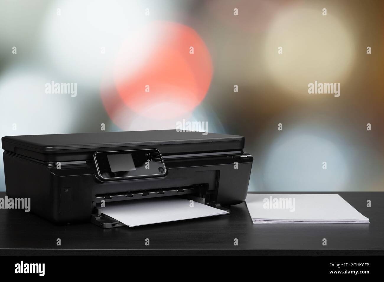 Compact laser printer on black desk against blurred background Stock Photo
