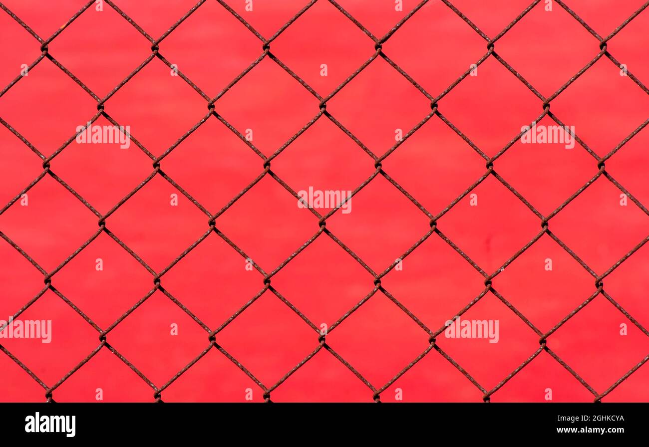 Rusty chain link fence on red blur background, shallow focus Stock