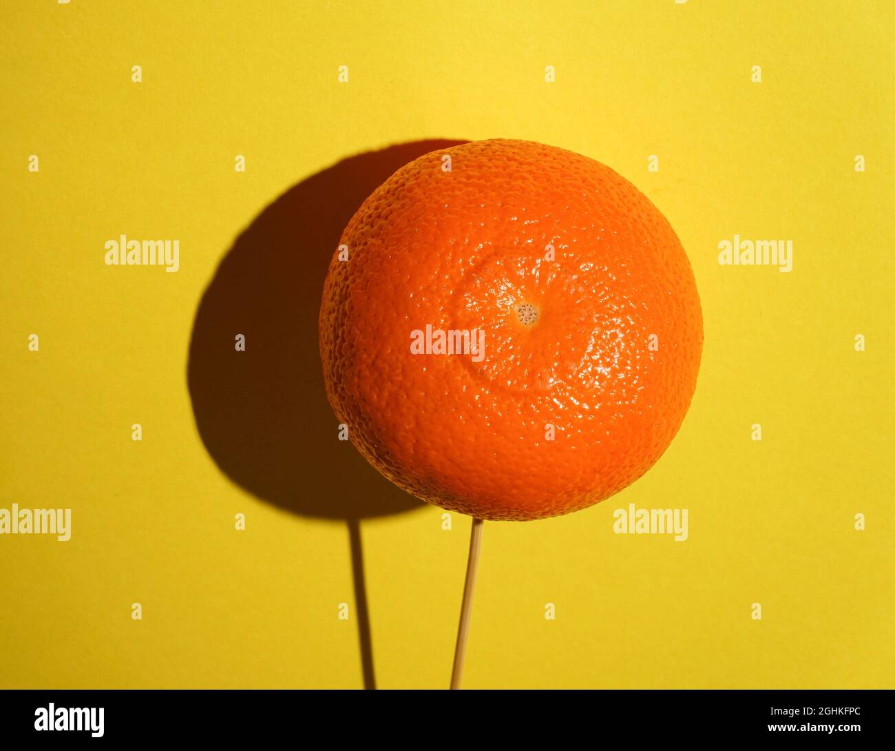 Ripe juicy orange mandarine tangerine as fruit Candy lollipop on bright yellow background with deep hard shadow. Stock Photo