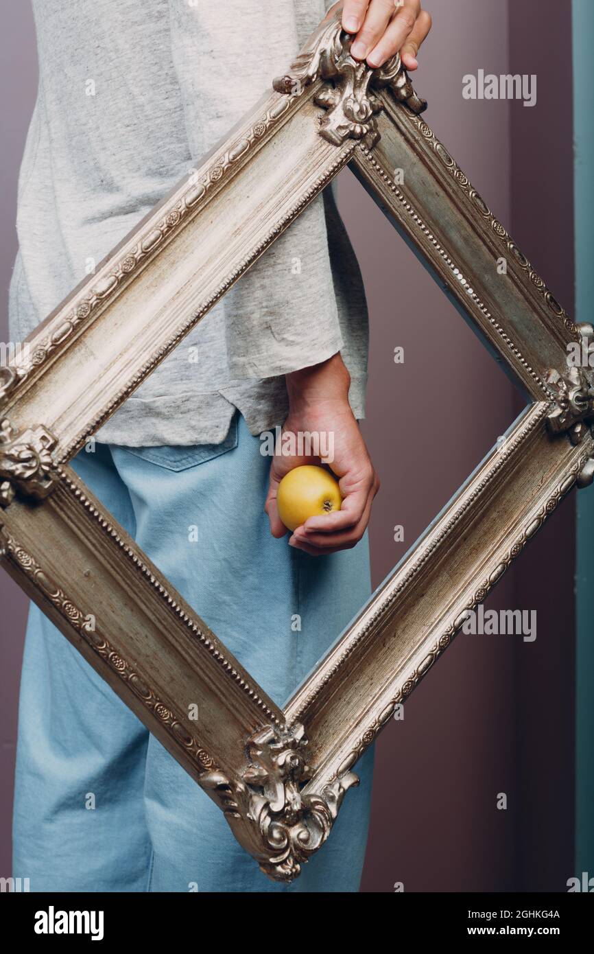 Millenial young man holds apple on hand palm in gilded picture frame Stock Photo