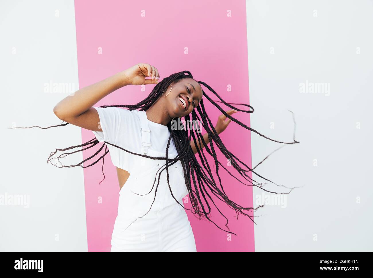 Dance Braid Playful woman with long braided hair dancing at a white wall with pink ...
