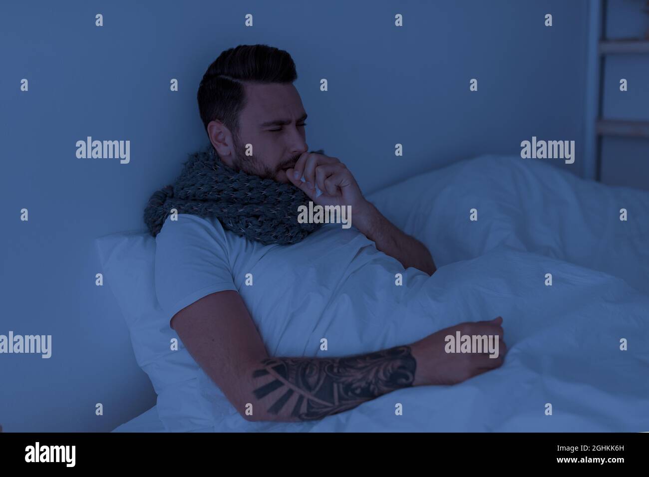Coronavirus, influenza concept. Sick young man coughing, holding paper napkin near mouth, sitting in bed at night Stock Photo