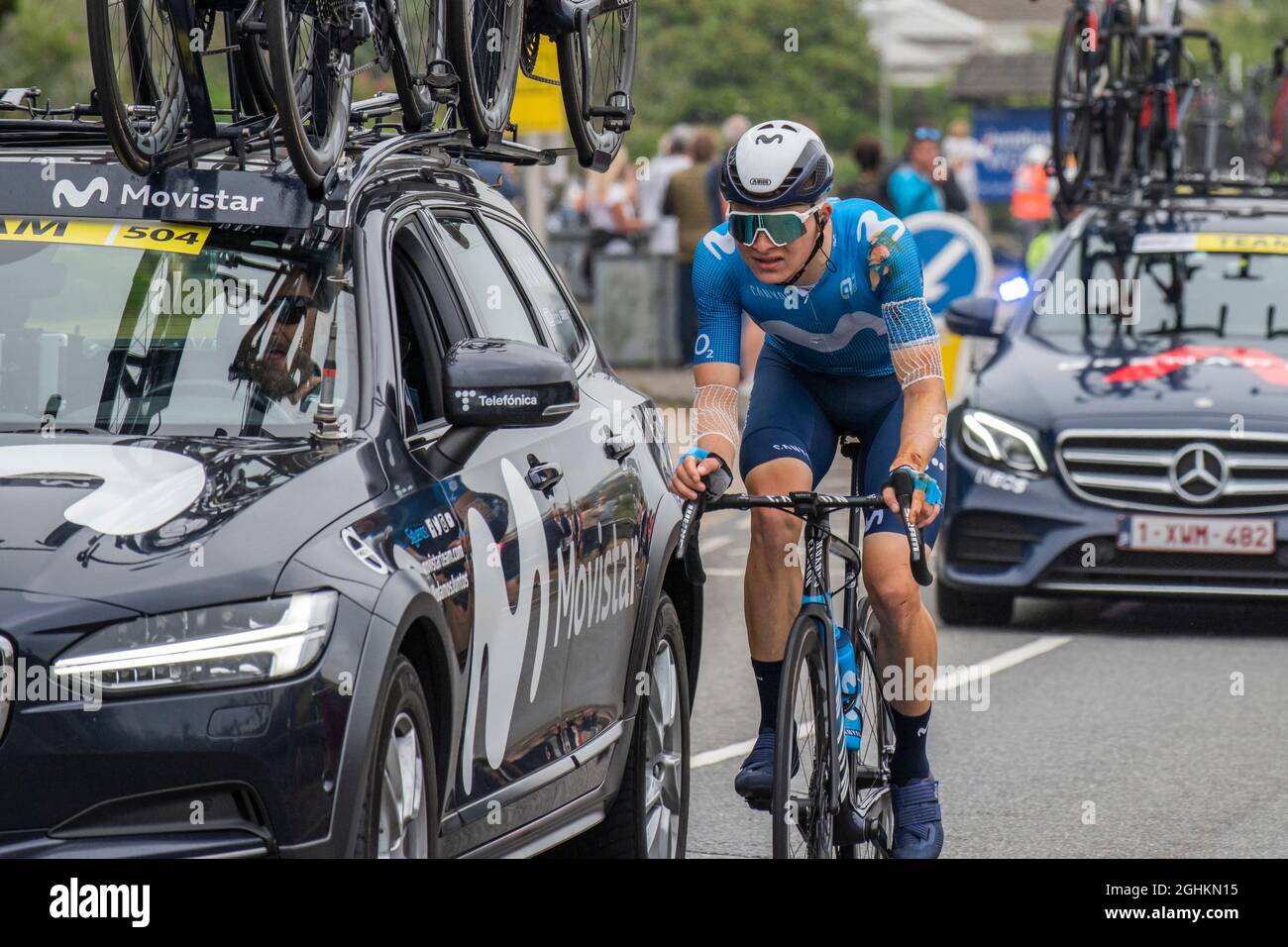 An injured rider from the Movistar Team Riding alongside a support vehicle car in the opening stage of the iconic Tour of Britain 2021 - known as The Stock Photo