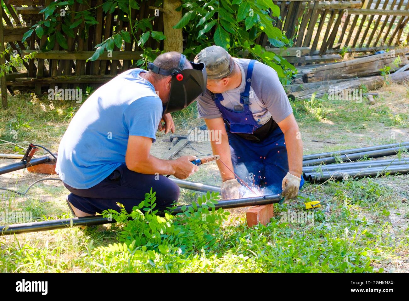 Workers weld metal pipes with electric arc welding on a sunny summer