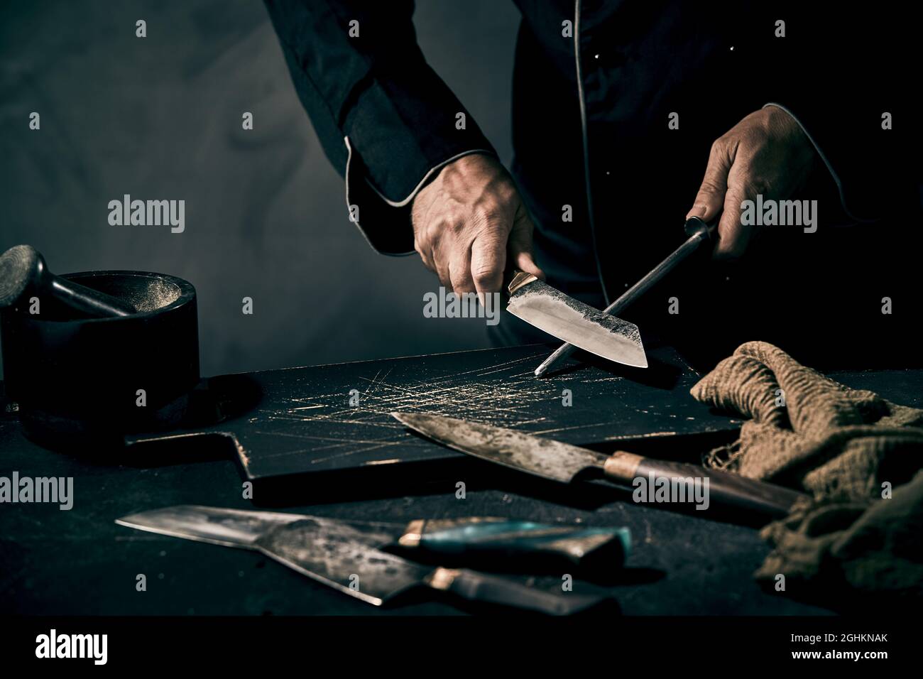 https://c8.alamy.com/comp/2GHKNAK/chef-or-butcher-sharpening-his-knife-with-an-old-fashioned-handheld-metal-file-over-on-old-black-cutting-board-in-low-angle-in-dim-light-with-copyspac-2GHKNAK.jpg