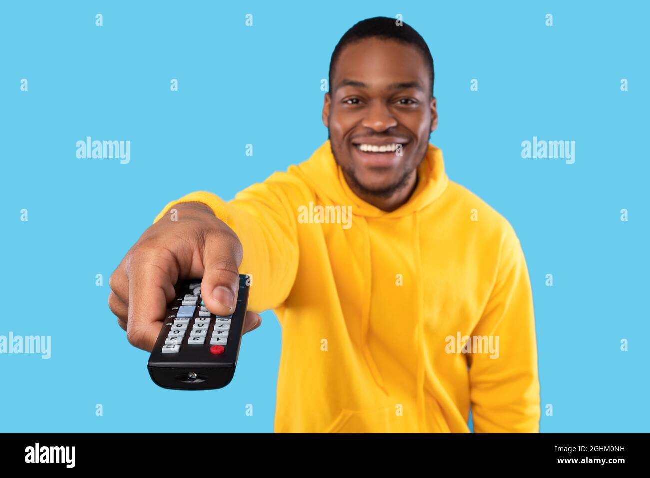 Cheerful Black Guy Watching TV Pointing Remote Controller, Blue Background Stock Photo