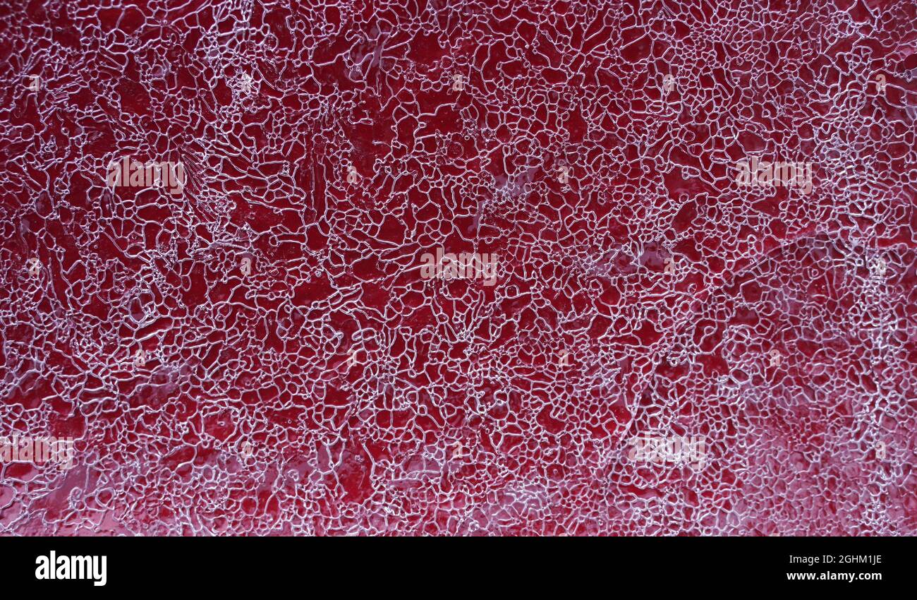 Cracked ice on a red metal surface as background. Selective focus. Stock Photo